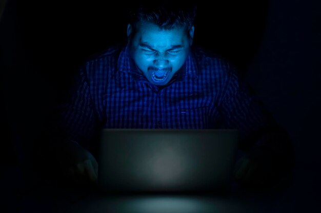 Hacker gritando o gritando contra la pantalla del portátil en la noche