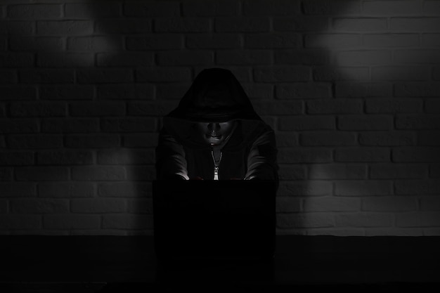 Hacker in schwarzer Maske und Kapuze am Tisch