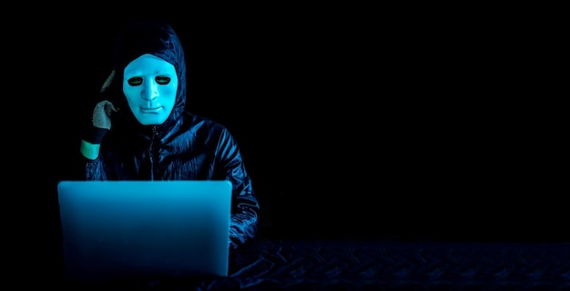 Hacker in weißer Maske und Hoodie, der mit einem Laptop im Internet surft und ernsthaft über Fragen, Terroristen und virtuellen Raum nachdenkt. Unsicheres Zonenkonzept, sehr verwirrte Idee