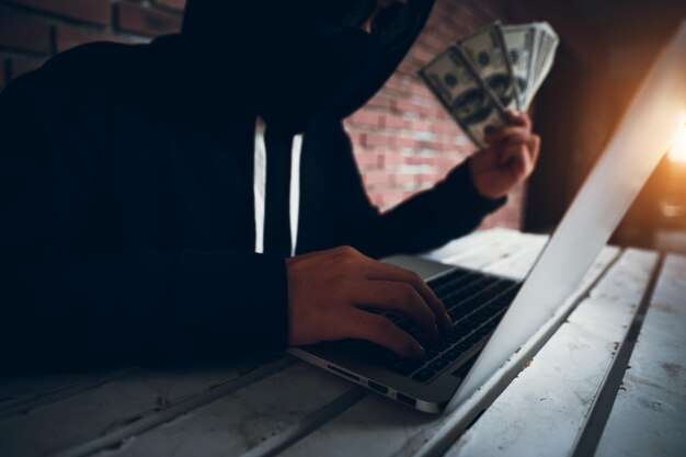 Foto hacker informático que nos sostiene dinero de papel mientras usa una computadora portátil