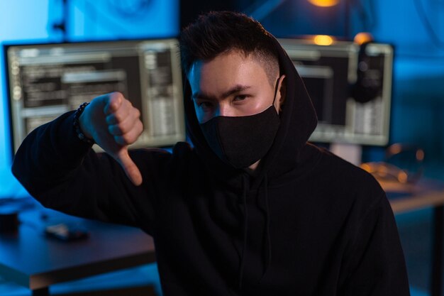 Hacker masculino con máscara mostrando los pulgares hacia abajo gesto