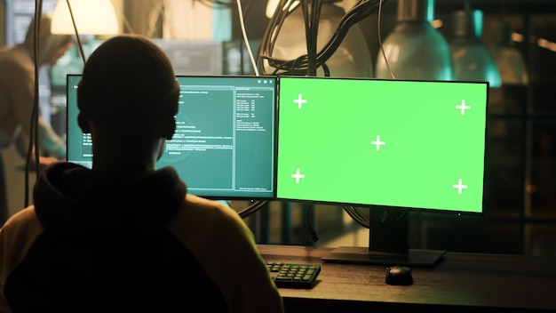 Un hacker masculino usa una pantalla verde para hackear un servidor en línea, planeando un ataque de phishing a altas horas de la noche. Joven haciendo actividad ilegal con plantilla de clave de croma aislada y espacio de copia, violación de seguridad.