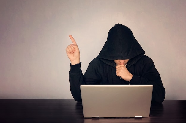 Hacker mit Kapuze vor seinem Computer zeigen Finger. Dunkles Gesicht. Hooded .technology Konzept, Hacker zeigt mit dem Finger auf leeren Raum für Text.