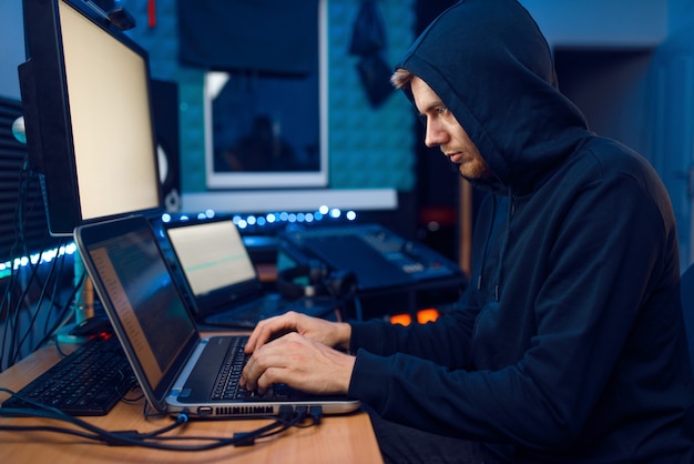 Hacker no capô sentado no laptop, hacking de informações. Espião da Internet, programador do sexo masculino tentando hackear uma rede criptografada