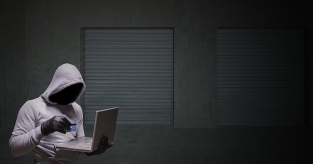 Hacker puente gris con la computadora y la tarjeta de crédito en una esquina