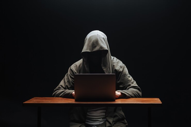 Foto hacker sin rostro en un capó con una computadora portátil sobre un fondo negro