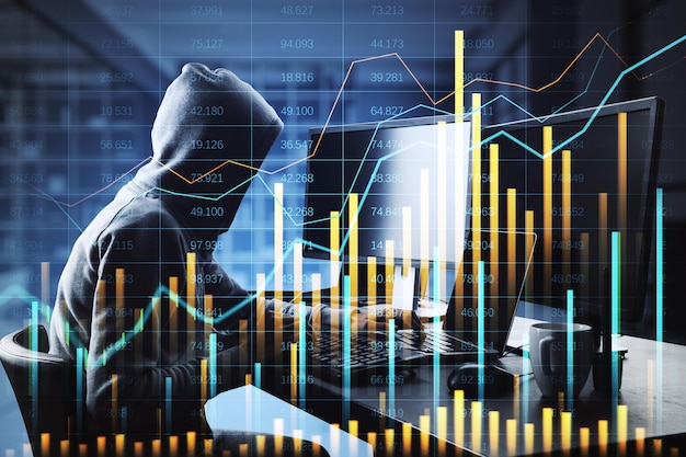 Hacker con una sudadera con capucha escribiendo en una computadora portátil con gráficos financieros y superposiciones de datos