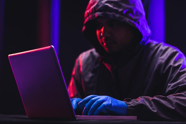 Hacker tragen Kapuzen, um ihr Gesicht zu bedecken. Hacking, um wichtige Informationen zu stehlen. Verwenden Sie einen Computer, um Malware-Viren freizusetzen und Organisationen zu belästigen. Er sitzt im dunklen Raum mit Neonlicht