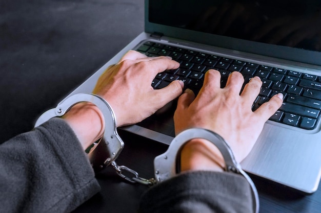 Hackerhände benutzen Laptop und sind mit Handschellen gefesselt