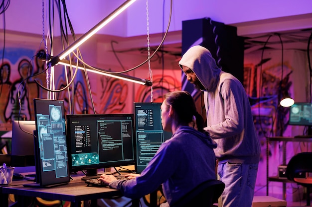 Hackers que codifican software malicioso en una computadora mientras trabajan en un almacén abandonado. Ladrones de Internet encapuchados planean ataques de phishing y programan malware en un cuarto oscuro