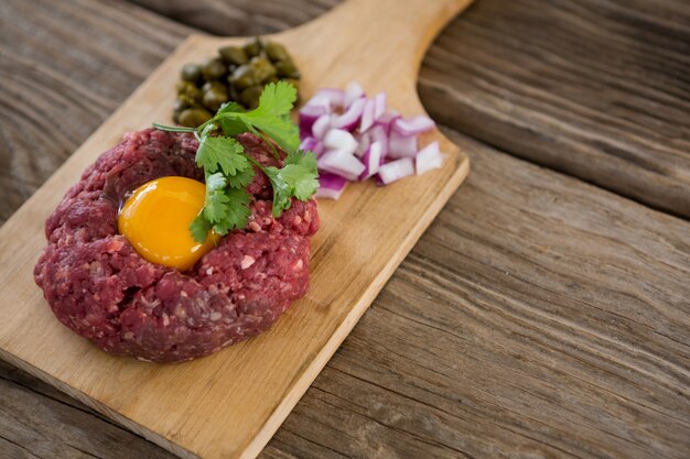 Foto hackfleisch mit eigelb, zwiebeln und oliven auf holztablett