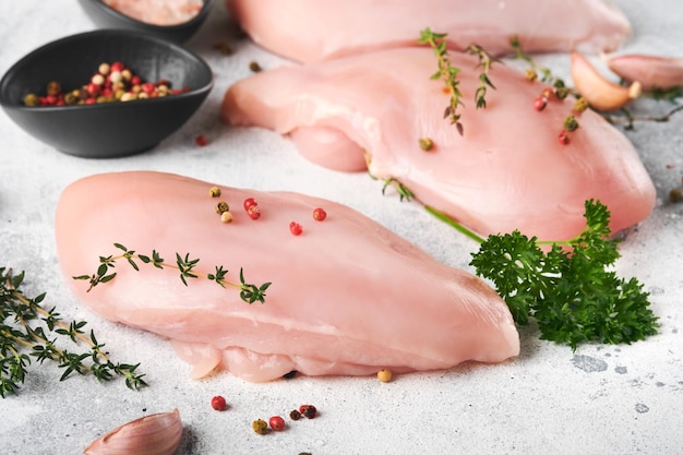 Hähnchenbrust Rohe Hähnchenbrustfilets auf schwarzer Keramikplatte auf Holzschneidebrett mit Kräutern und Gewürzen auf altem grauem Tischhintergrund Draufsicht mit Kopierraum