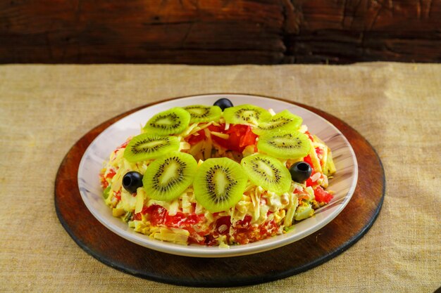 Hähnchenbrustblätterteigsalat, garniert mit Kiwi und Oliven in einer Salatschüssel auf einer Tischdecke.