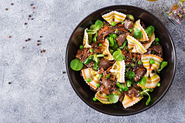 Hähnchenherzen mit Möhren in süß-saurer Sauce mit Farfalle-Nudeln. Gesunder Salat. Ansicht von oben. Flach liegen.