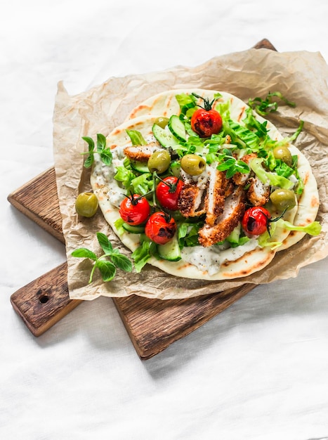 Hähnchenschnitzel griechischer Gyros mit Kopfsalat Tzatziki-Sauce gerösteten Tomaten Gurken Oliven auf einem Schneidebrett auf hellem Hintergrund Draufsicht