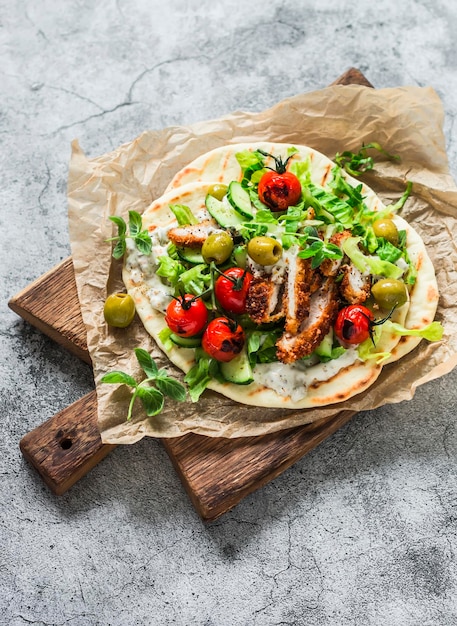 Hähnchenschnitzel griechischer Gyros mit Kopfsalat Tzatziki-Sauce gerösteten Tomaten Gurken Oliven auf einem Schneidebrett auf hellem Hintergrund Draufsicht