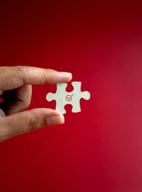 Häkchen-Symbol auf einem Puzzleteil Puzzle-Element in der Hand des Menschen isoliert auf rotem Hintergrund vertikal minimaler Stil Business-Lösung löst Mission Partnerschaftserfolg und Strategiekonzepte