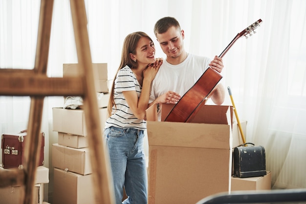 Hält Akustikgitarre in den Händen. Fröhliches junges Paar in ihrer neuen Wohnung. Konzeption des Umzugs.