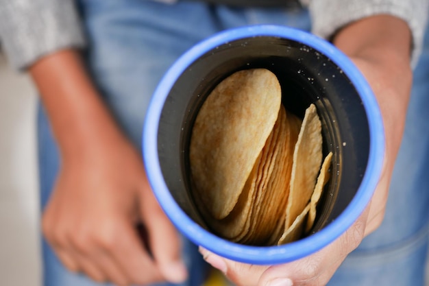 Hält einen Plastikbehälter voller Kartoffelchips