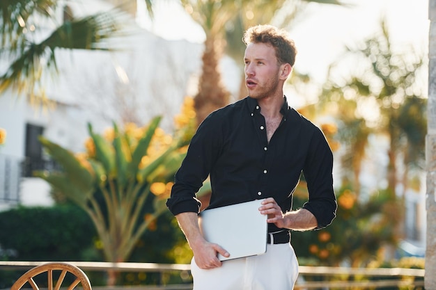 Hält Laptop Junger Mann ist tagsüber im Freien Konzept des Urlaubs