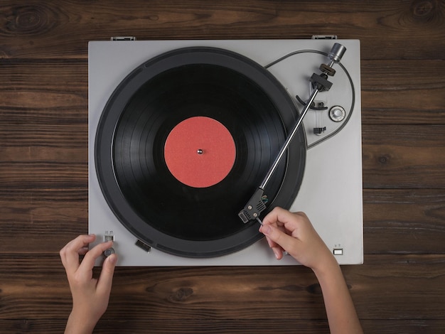Hände auf Vinyl-Plattenspieler auf einem hölzernen Hintergrund