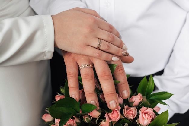 Hände der Braut und des Bräutigams mit Goldringen des Hochzeitsblumenstraußes
