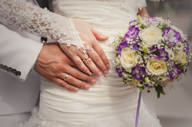 Hände der Braut und des Bräutigams mit Hochzeitsblumenstrauß und -ringen