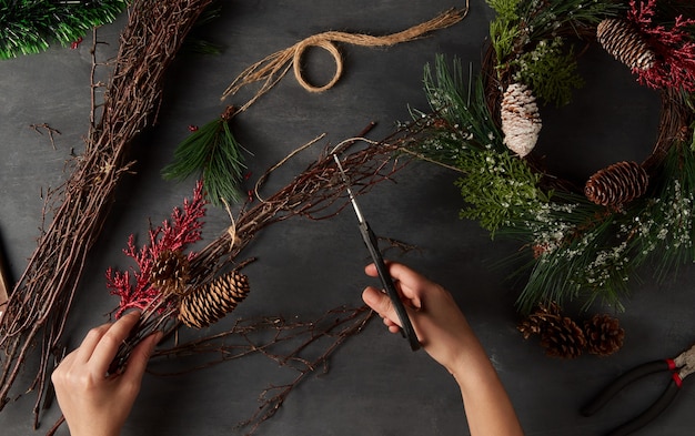 Foto hände der frau, die eine weihnachtskrone in einem dunklen hintergrund basteln, diy