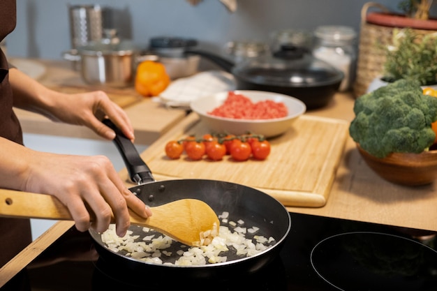 Hände der jungen Frau, die gehackte Zwiebel in der Bratpfanne mischt