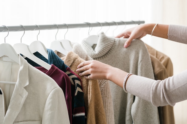 Hände der jungen Käuferin, die warme Strick- und Wollkleidung aus der neuen saisonalen Freizeitkollektion auswählt