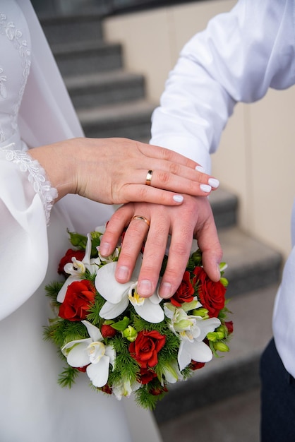 Hände der Jungvermählten auf einem Hochzeitsstrauß aus Rosen und Orchideen Konzept für Agenturen