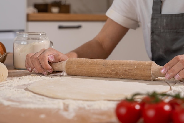 Hände der Konditorfrau, die Teig mit Nudelholz auf dem Tisch ausrollt