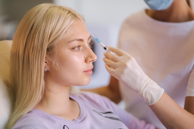 Hände der Kosmetikerin, die Injektionen in die Gesichtslippen macht Junge Frau bekommt Schönheits-Gesichtsinjektionen in der medizinischen Klinik