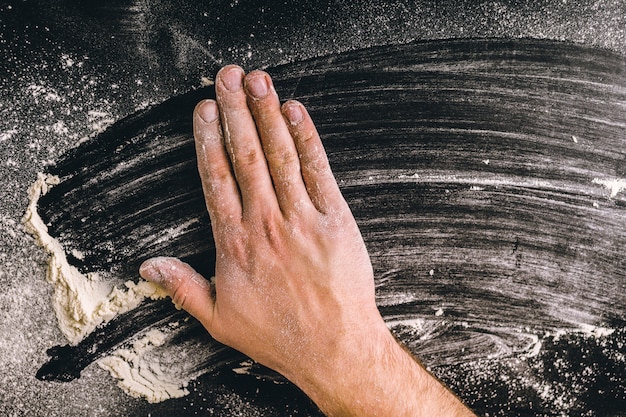 Hände des erwachsenen Mannes arbeiten mit Mehl, dunkles Foto