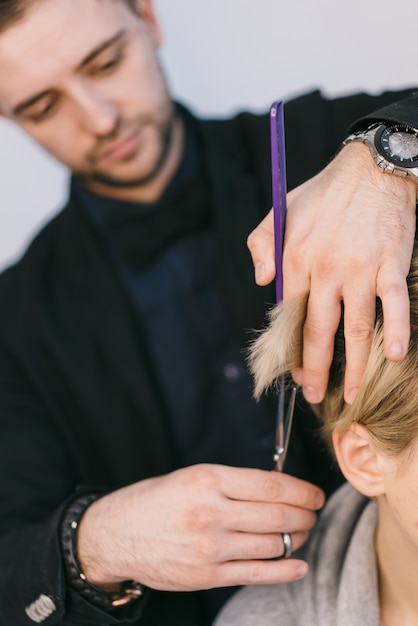 Hände des Friseurs schneiden Haar der Blondine mit der Anwendung von Scheren in einem Schönheitsstudio. Nahansicht