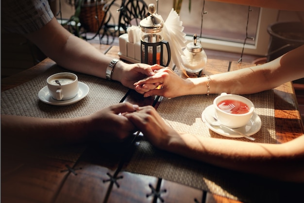 Foto hände des kerls und hand des mädchens an einem tisch mit einer tasse tee und einem tasse kaffee im caféshop