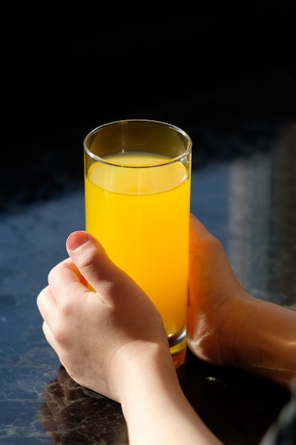 Hände des Kindes, das Glas mit Orangensaft hält