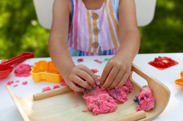 Hände des kleinen Mädchens, das mit kinetischer Sandnahaufnahme spielt. Freizeitaktivität im Freien am Sommertag.