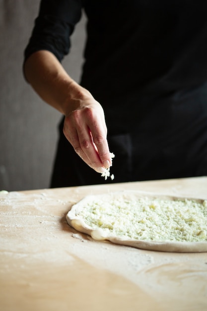 Hände des Kochs bereiten Pizza vor. Gießt Käse auf den ausgerollten Teig