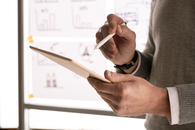 Foto hände des männlichen maklers oder ökonomen mit stift, der auf touchpad-anzeige zeigt, während er gegen whiteboard steht