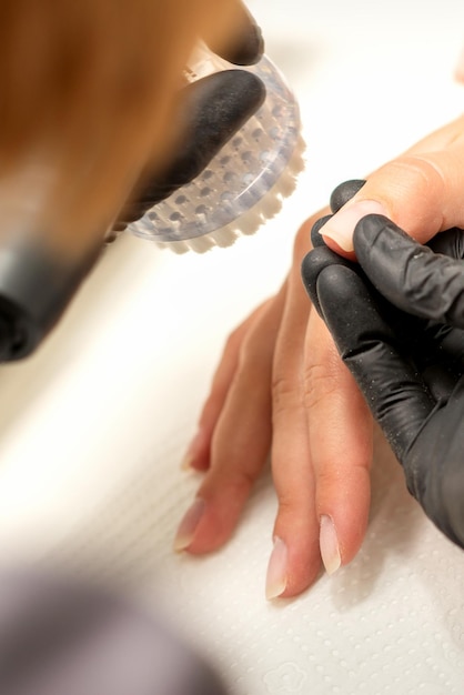 Hände des Maniküremeisters entfernen Staub von Nägeln mit einer Bürste, die Nägel in einem Nagelstudio reinigt