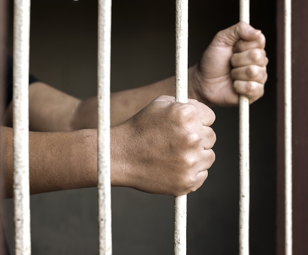 Hände des Mannes Gefangenen Greifen in und out auf rostigen Gefängnis Bars
