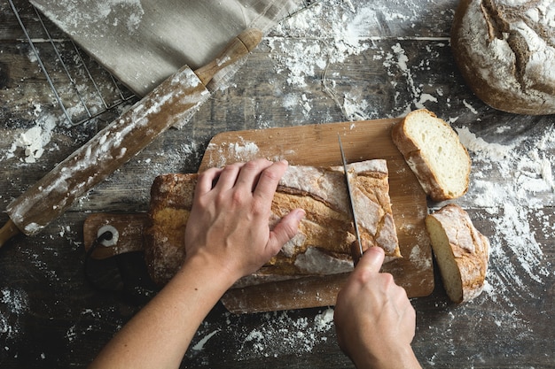 Hände, die Brot auf Holztisch schneiden