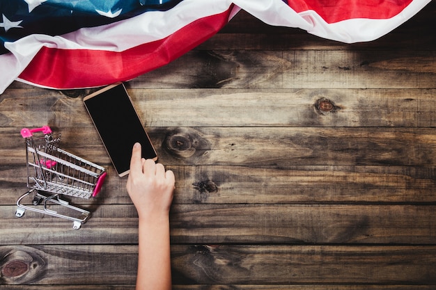 Hände, die ein Smartphone auf einem hölzernen Hintergrund mit einer Flagge von USA berühren.