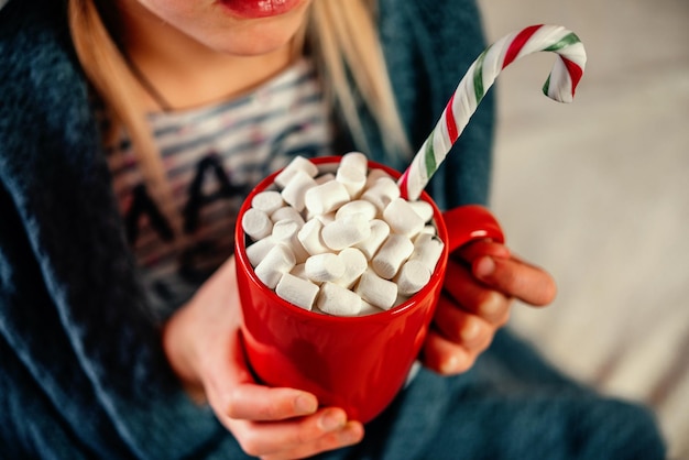 Hände, die eine rote Tasse heiße Schokolade mit Marshmallows-Weihnachtshintergrund halten