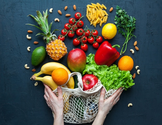 Hände, die eine schnurtasche mit gesundem vegetarischem essen halten vielfalt an gemüse und obst