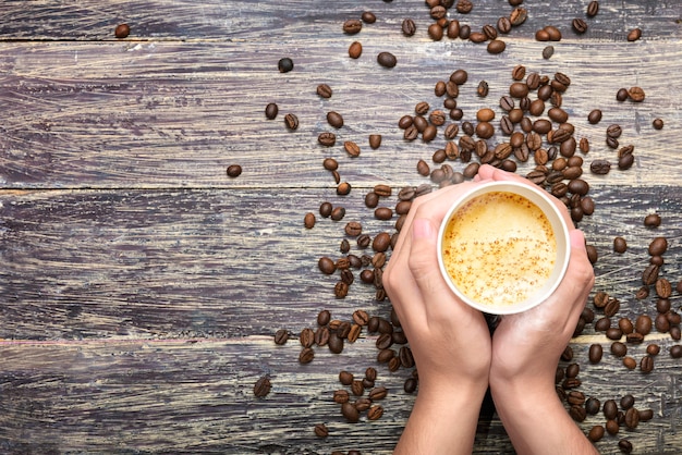 Hände, die eine Tasse heißen Kaffee mit Kaffeebohnen halten