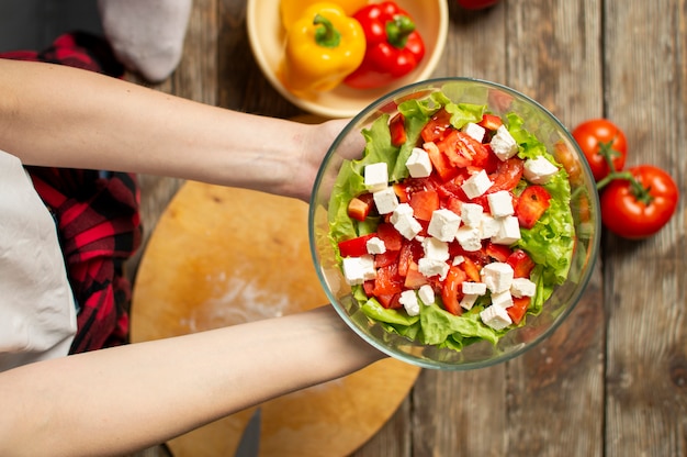 Hände, die einen vegetarischen Salat in einer Glasplatte halten