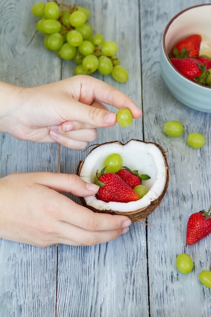 Hände, die Erdbeeren und Trauben in der Kokosnussschale stapeln