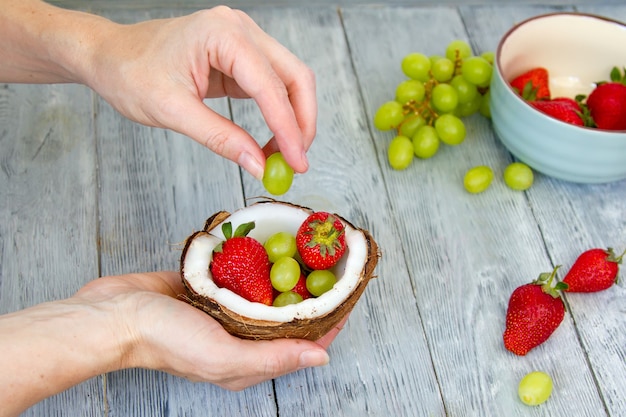 Hände, die Erdbeeren und Trauben in der Kokosnussschale stapeln